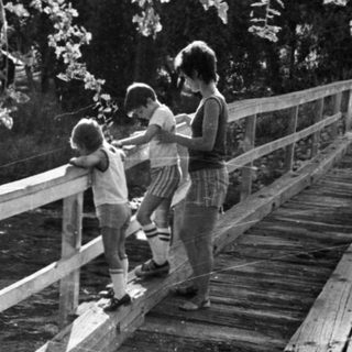 Family crossing a wooden bridge near water.