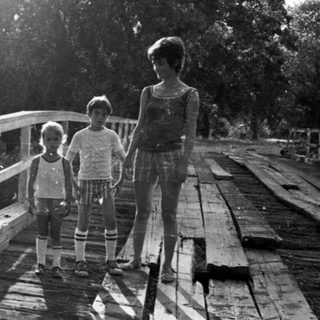 Family walking on a wooden bridge in sunlight.