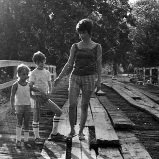Three people walking on a wooden bridge near water.