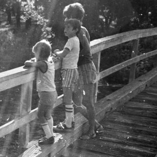 Two children standing on a wooden bridge in sunlight.