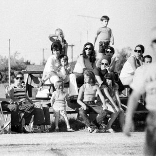 Group of people relaxing outdoors in 1970s-style clothing.