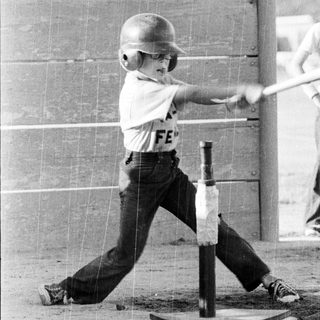 Young boy swinging baseball bat at tee.