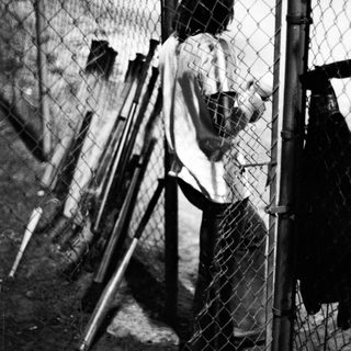 A person practices baseball batting near chain-link fence.