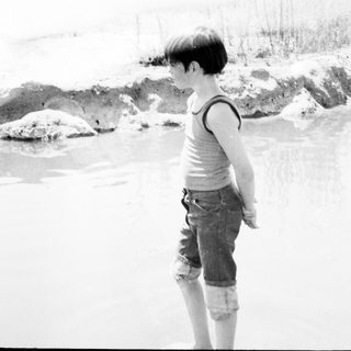 Child with blue hair standing near snow-covered rocks.