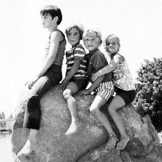 Four children sitting together on a large rock outdoors.