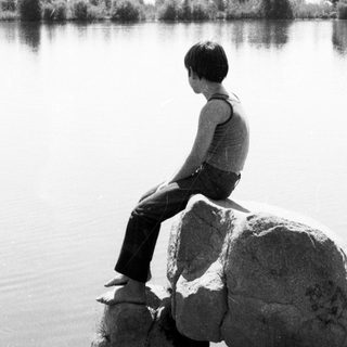 Person sitting on rocks by calm lake.