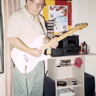 Man playing electric guitar indoors near stereo equipment.