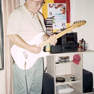 Man playing electric guitar indoors near stereo equipment.