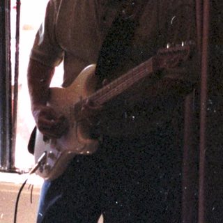 Man playing electric guitar in dimly lit room.