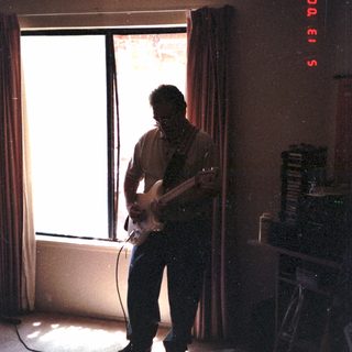 Man playing electric guitar in dimly lit room.