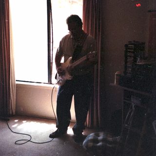 Man playing electric guitar in dimly lit room.