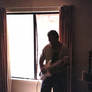 Man playing electric guitar in dimly lit room.