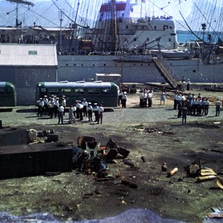 Port scene with shipwreck debris and workers inspecting damage.