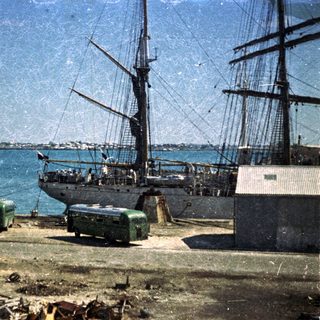 Historic sailing ship docked at coastal pier.