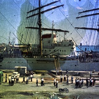 Historic port scene with large sailing ships and dockworkers.