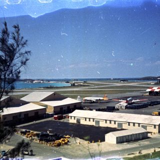 Small airport terminal with aircraft, runway, and ocean backdrop.