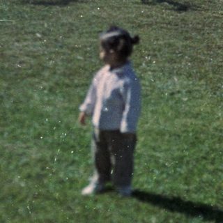Young child standing alone in grassy backyard.