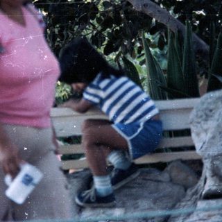 Woman carrying items, child sitting near cactus.
