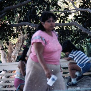 Woman carrying items, child sitting near cactus.