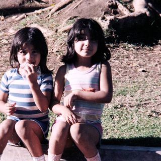 Two young girls sitting outdoors eating.
