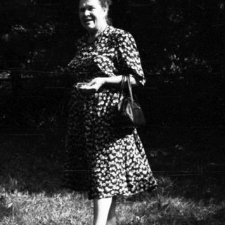 Woman standing beside haystack, child lying on grass.