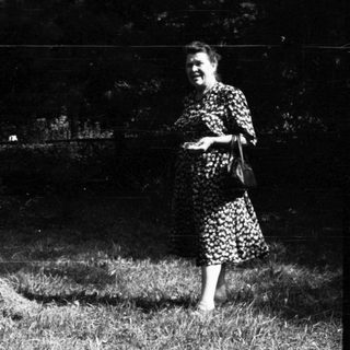 Woman standing beside haystack, child lying on grass.