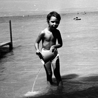 Shirtless boy playing in shallow water near dock.