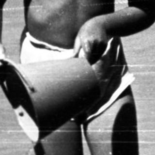 Shirtless boy playing in shallow water near dock.