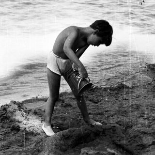 Shirtless boy digging near water's edge.