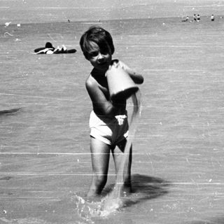 Children playing and wading in shallow water near dock.