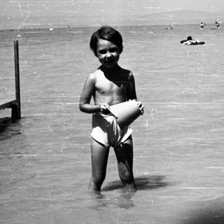 Child standing in shallow water near dock.