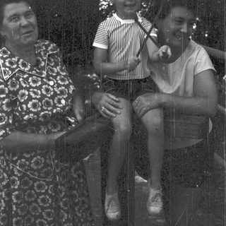 Three people sitting together outdoors in vintage clothing.