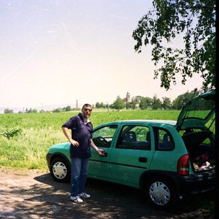 Man standing beside open hatch of green car in rural field.
