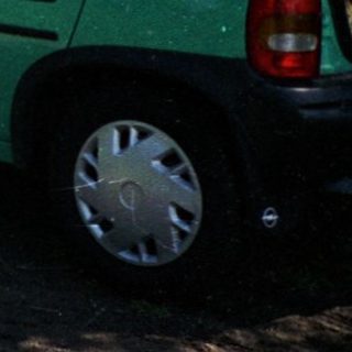 Man standing beside open hatch of green car in rural field.