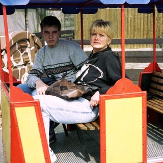 Two people riding a small, open train cart at zoo.