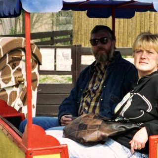 Two people riding a colorful train cart near zoo animals.