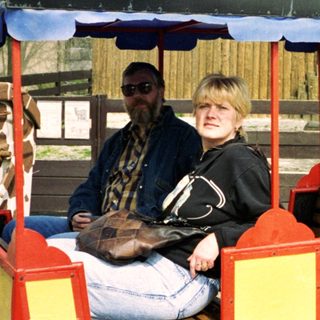 Two people riding a colorful train cart near zoo animals.