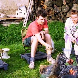 Two people grilling meat over an outdoor fire pit.
