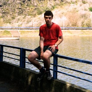 Young man sitting on bridge by lake.
