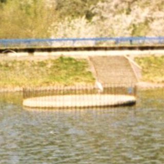 Scenic lake with grassy hill and bridge.
