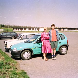 Two people posing beside a turquoise car.