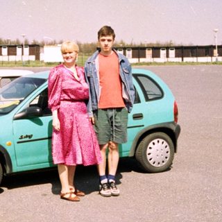 Two people posing beside a turquoise car.