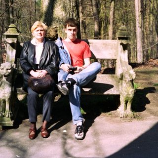 Two people sitting on bench in wooded park area.