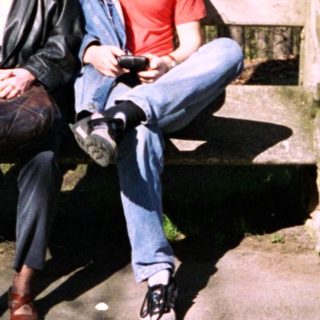 Two people sitting on bench in wooded park area.