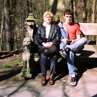 Two people sitting on bench in wooded park area.