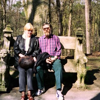 Two people sitting on park bench in wooded area.