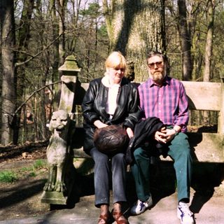 Two people sitting on park bench in wooded area.