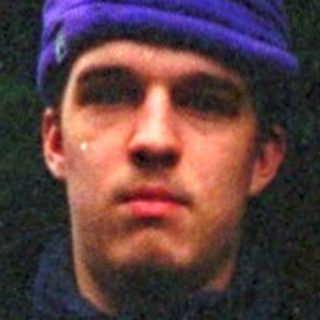Man standing outdoors in rain wearing purple beanie and jacket.