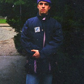 Man standing outdoors in rain wearing purple beanie and jacket.