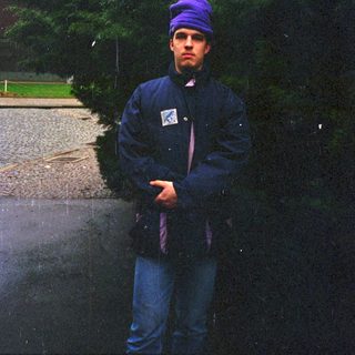 Man standing outdoors in rain wearing purple beanie and jacket.